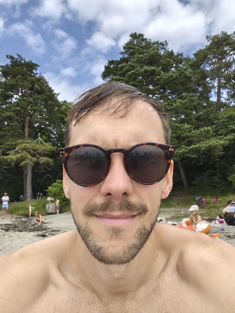Selfie av mann med solbriller på strand, fotografert med Motorola Edge 70s frontkamera